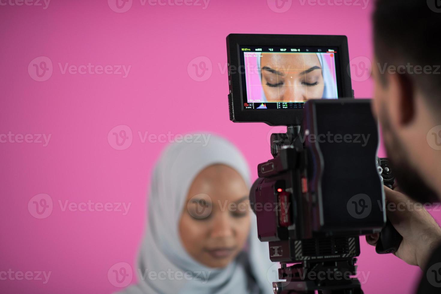 videógrafo en estudio rosa grabando video en cámara profesional disparando a mujer musulmana foto