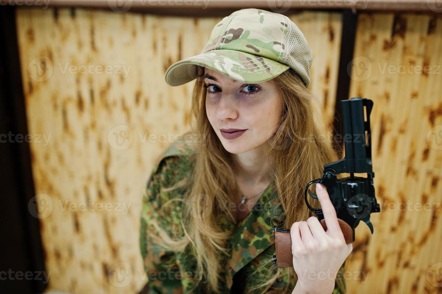 Military girl in camouflage uniform with revolver gun at hand against army background on shooting range. photo