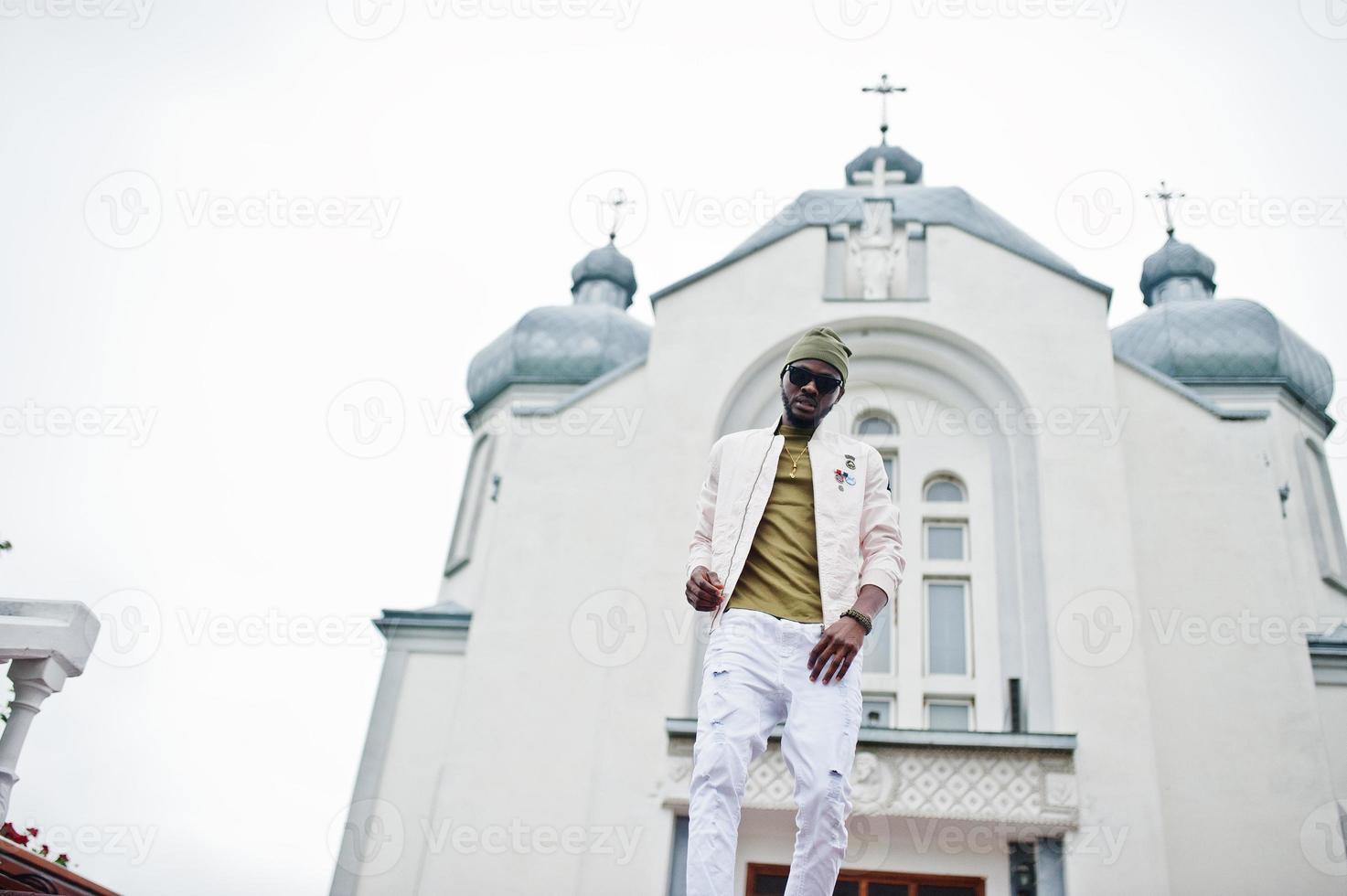 African american man in hat and sunglasses stand against church. Faith and Christianity in Africa. photo