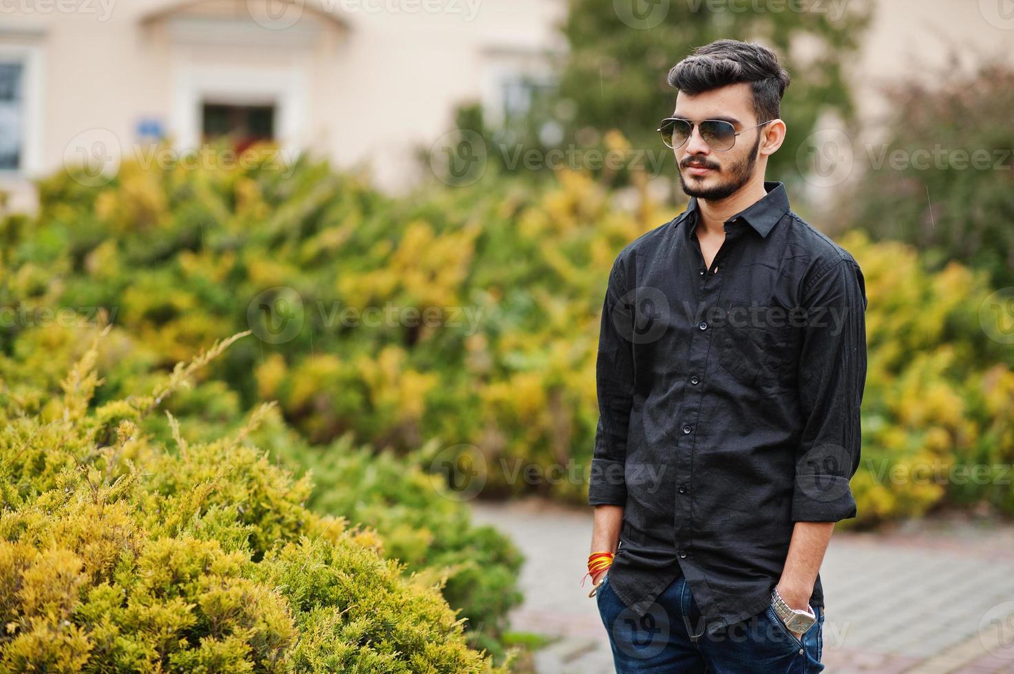 hombre con estilo indio en camisa negra y gafas de sol posó al aire libre. foto