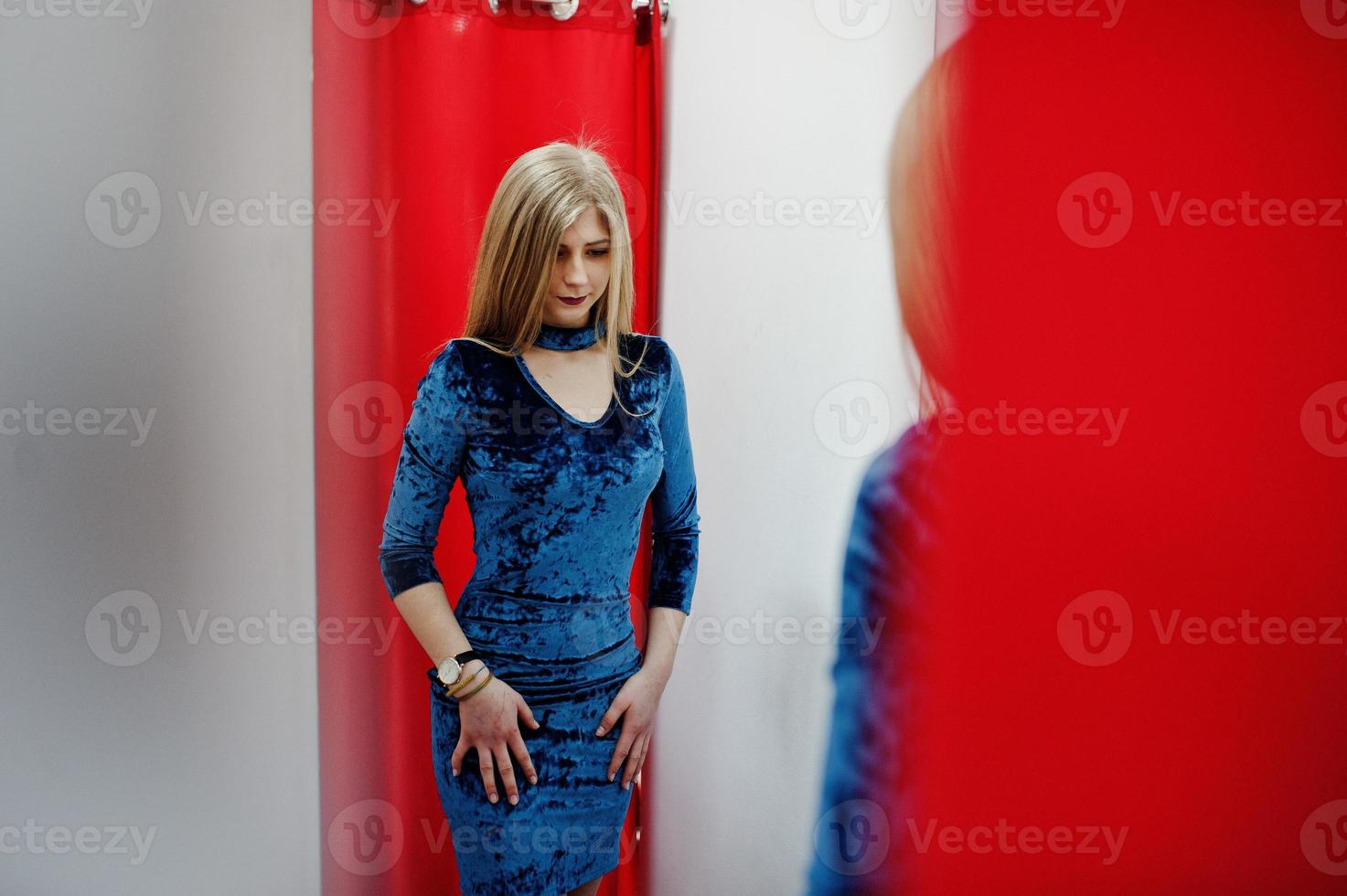 chica rubia con vestido azul en la tienda de ropa con cortinas rojas. foto