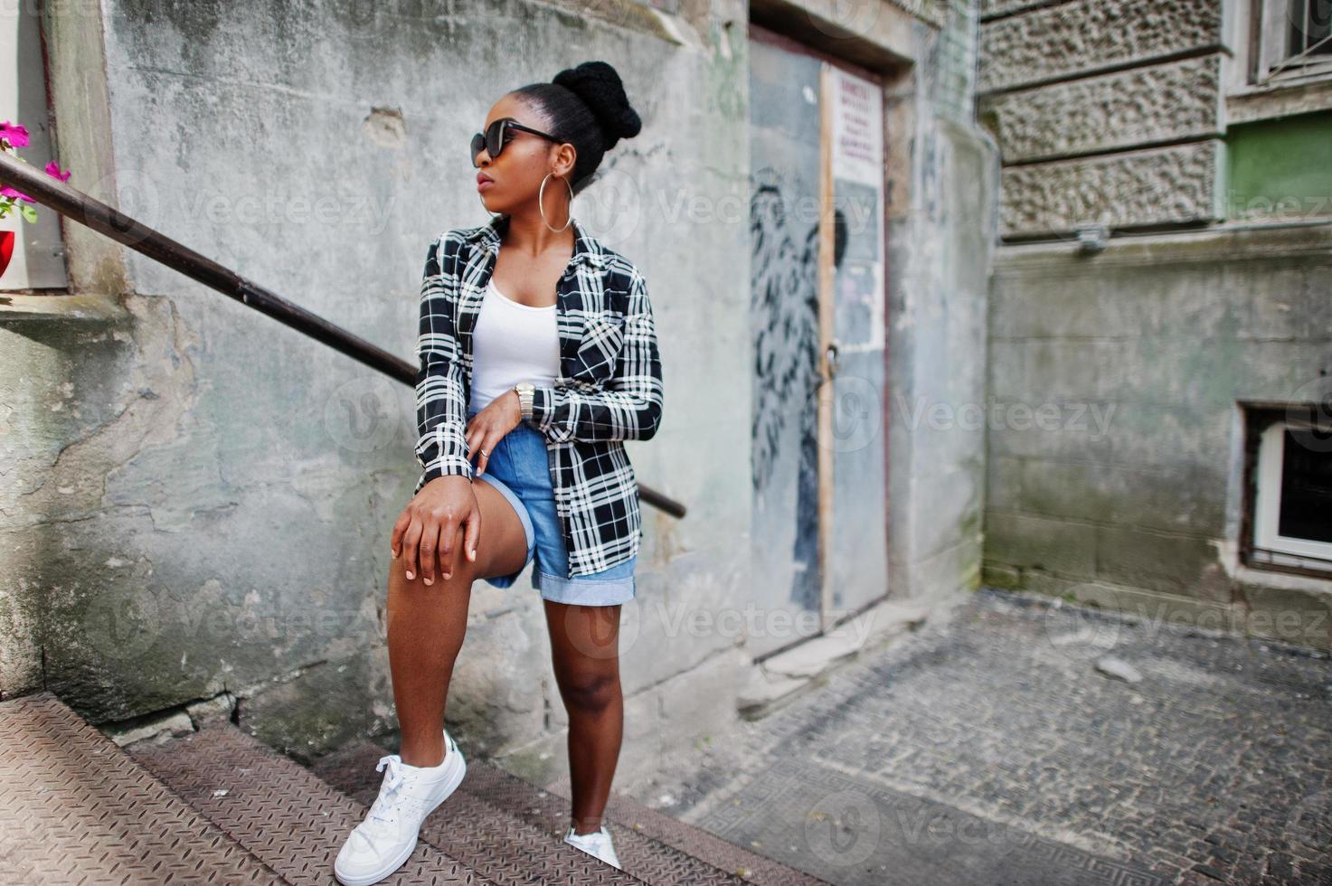 Hip hop african american girl on sunglasses and jeans shorts. Casual street fashion portrait of black woman. photo