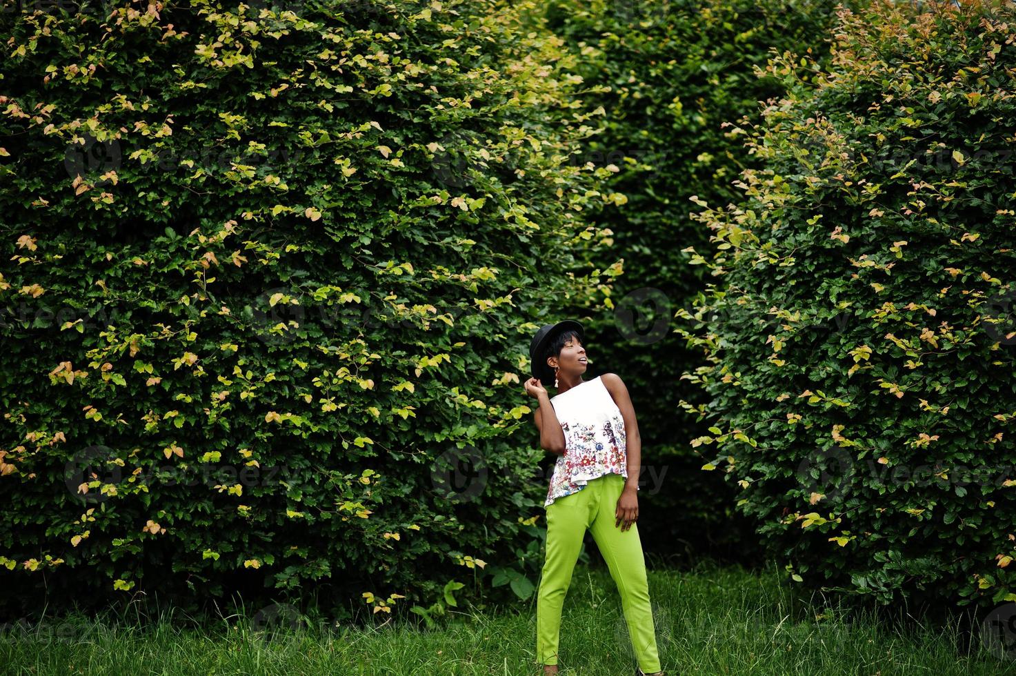 Amazing african american model woman in green pants and black hat posed at park. photo