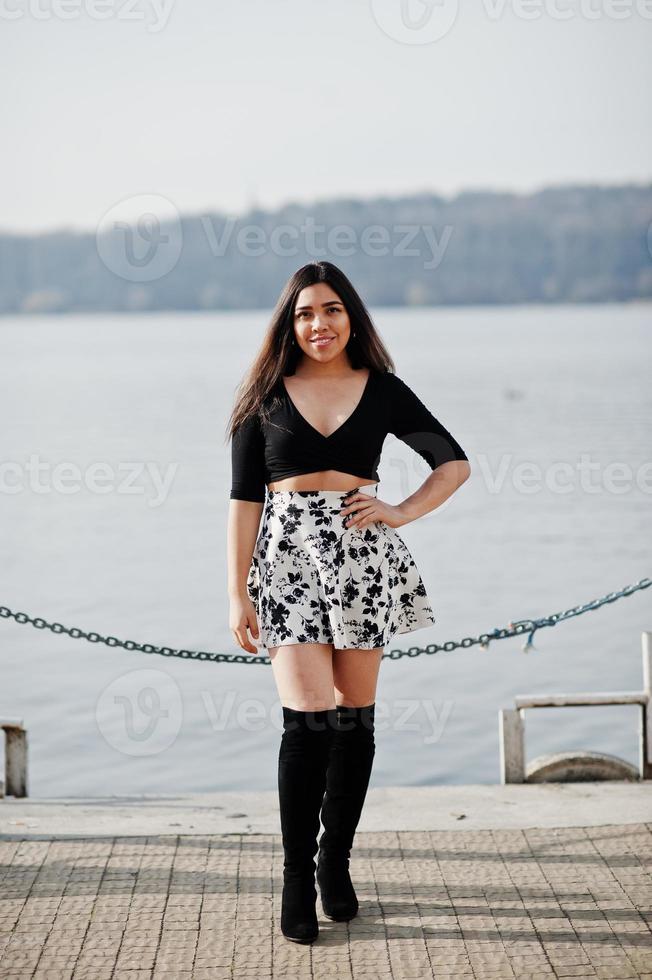 Pretty latino model girl from Ecuador wear on black tops and skirt posed against lake. photo