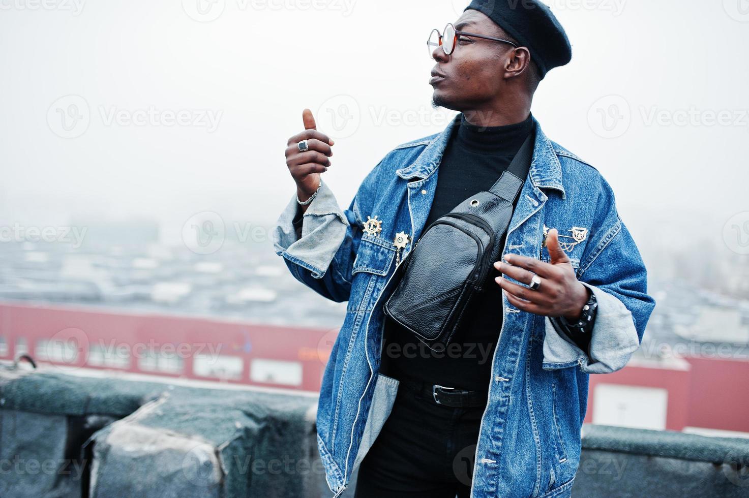 African american man in jeans jacket, beret and eyeglasses posed on abandoned roof. photo