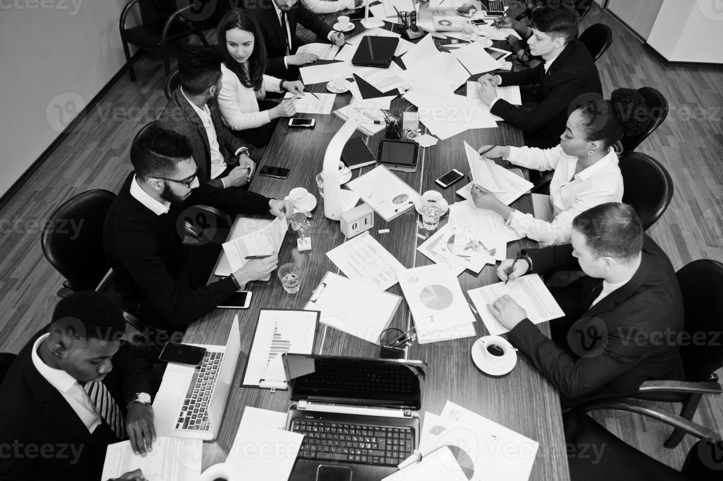 el equipo de negocios multirracial se dirige a la reunión alrededor de la mesa de juntas, trabaja juntos y escribe algo en los papeles. foto