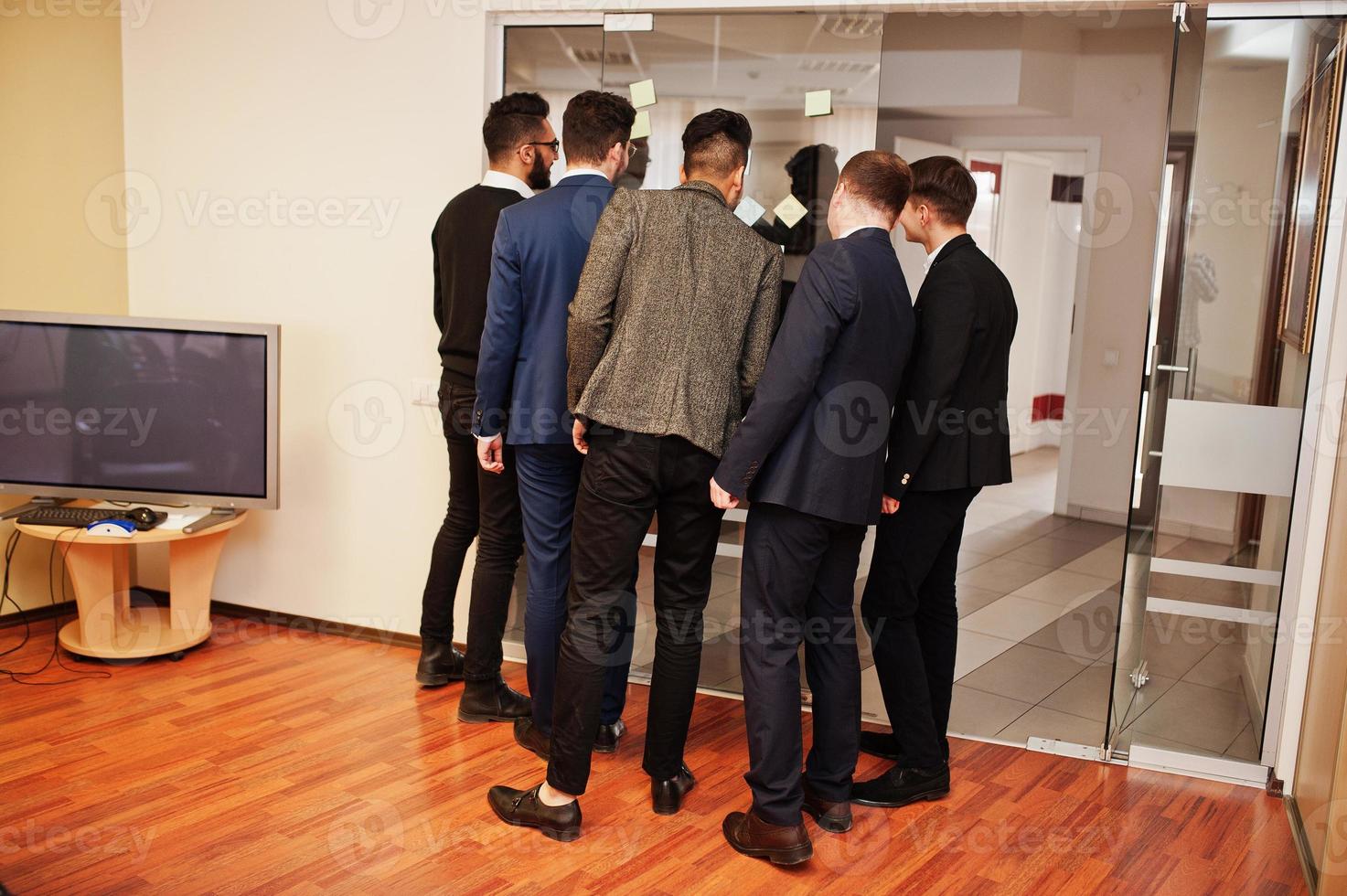 Business mans pointing on glass with colorful paper notes. Diverse group of male employees in formal wear using stickers. photo