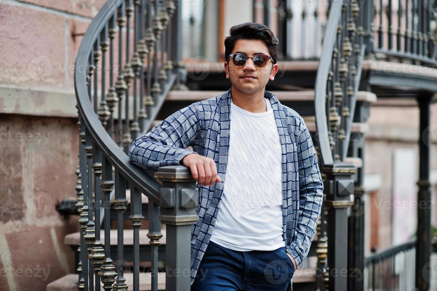 Stylish indian young man at sunglasses wear casual posed outdoor against iron stairs. photo