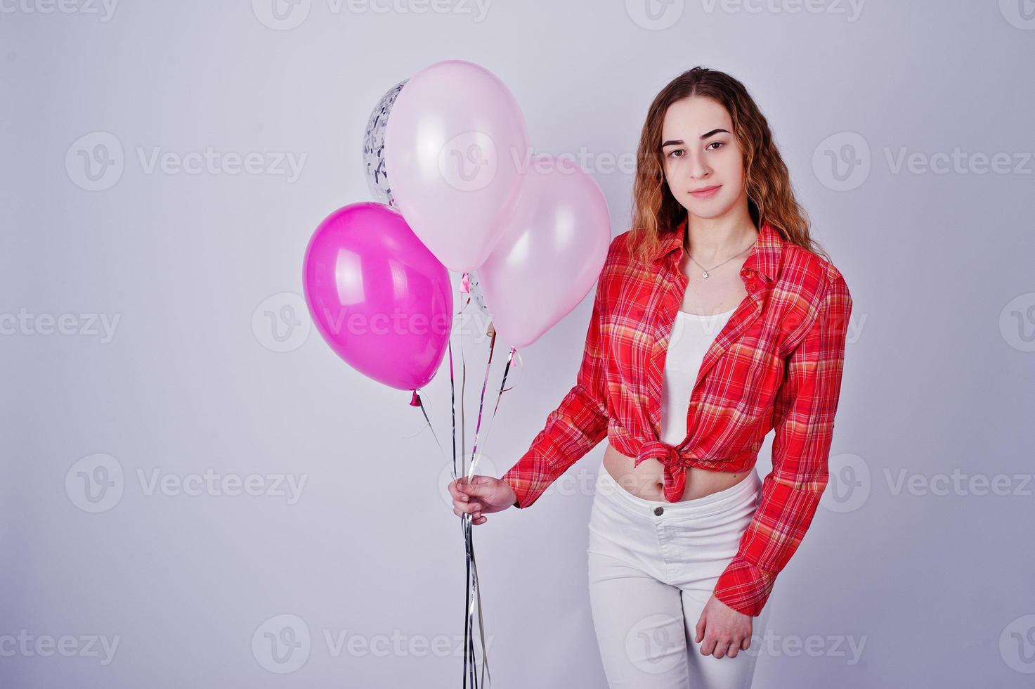 Young girl in red checked shirt and white pants with balloons against white background on studio. photo