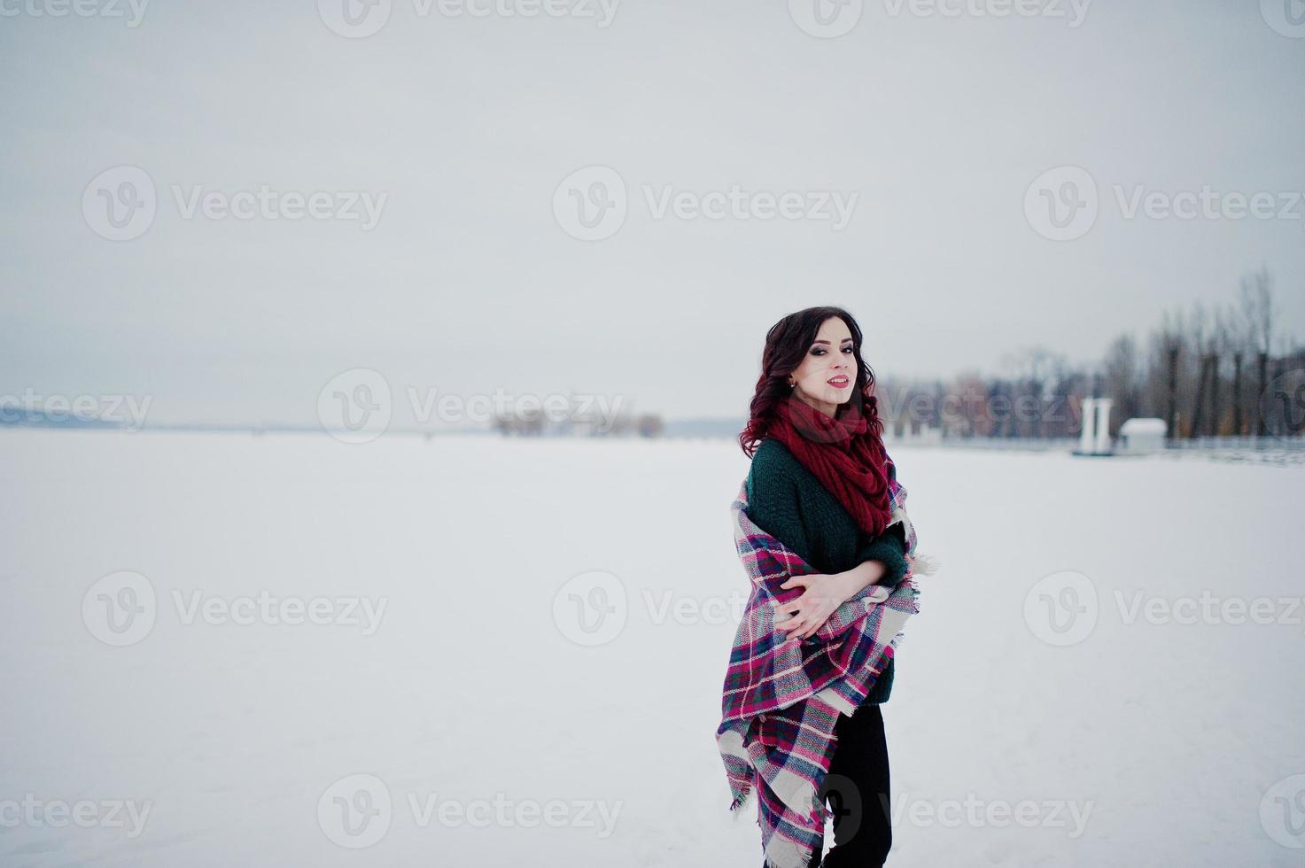 chica morena en suéter verde y bufanda roja con lago congelado al aire libre a cuadros en el día de invierno por la noche. foto