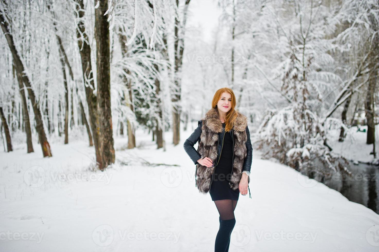 Red haired girl in fur coat walking at winter snowy park. photo