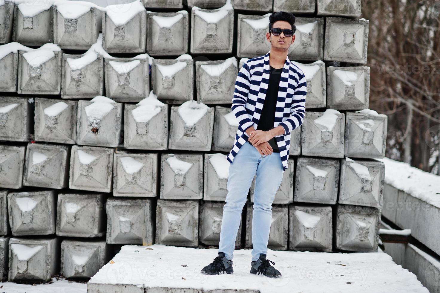 Casual young indian man in stripped sweater and sunglasses posed against stone blocks. photo