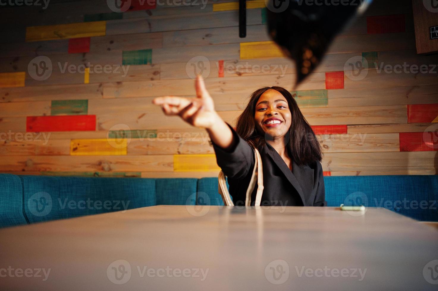 Charming african american woman model in black jacket relaxing in cafe during free time, throwing hat. photo