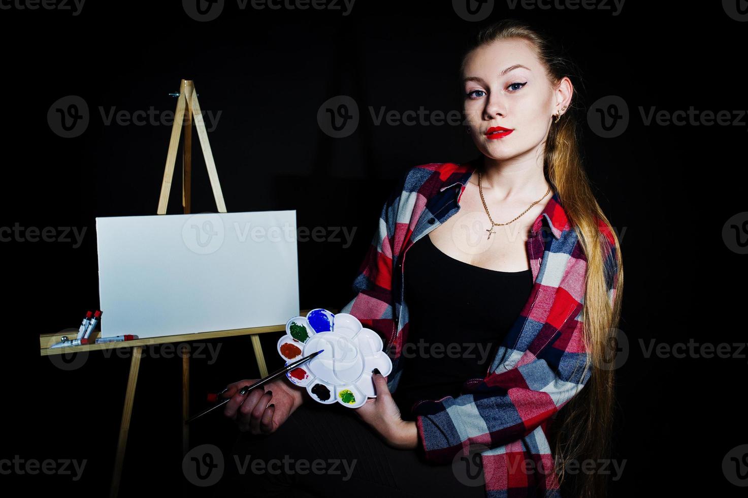 Beautiful woman artist painter with brushes and oil canvas posing in studio isolated on black. photo