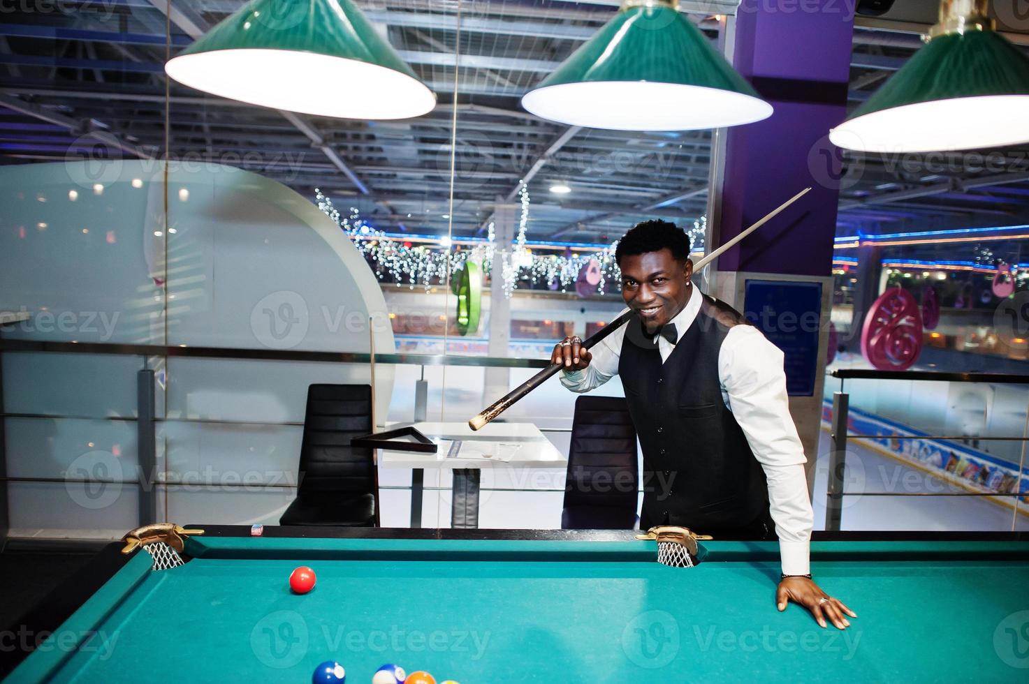 Young handsome african man wearing white shirt, black vest and bow tie play pool billiard. photo