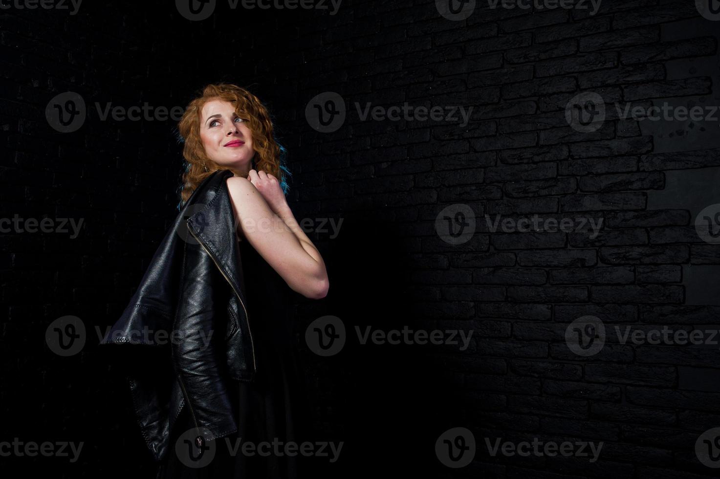 Curly hair girl at leather jacket on studio against black brick wall. photo