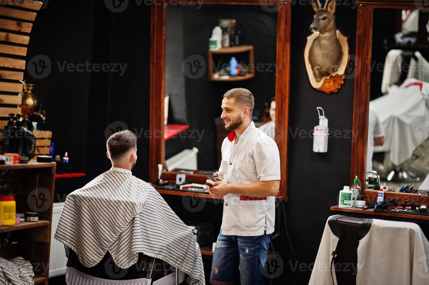 un joven barbudo que se corta el pelo con un peluquero mientras se sienta en una silla en la barbería. alma de barbero. foto