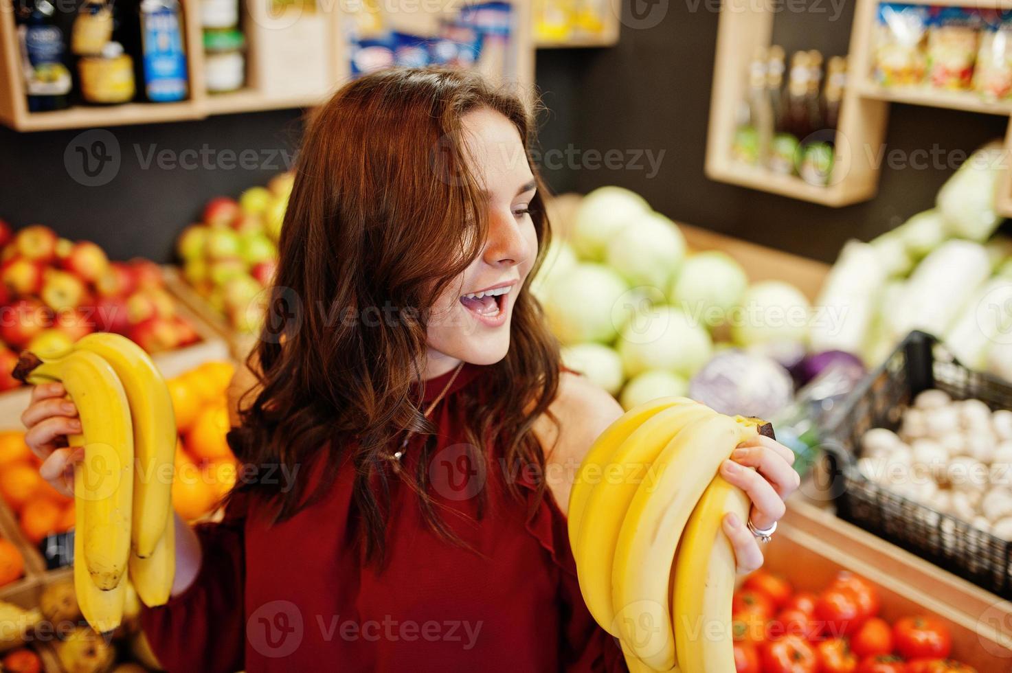 Girl in red holding bananas on fruits store. photo