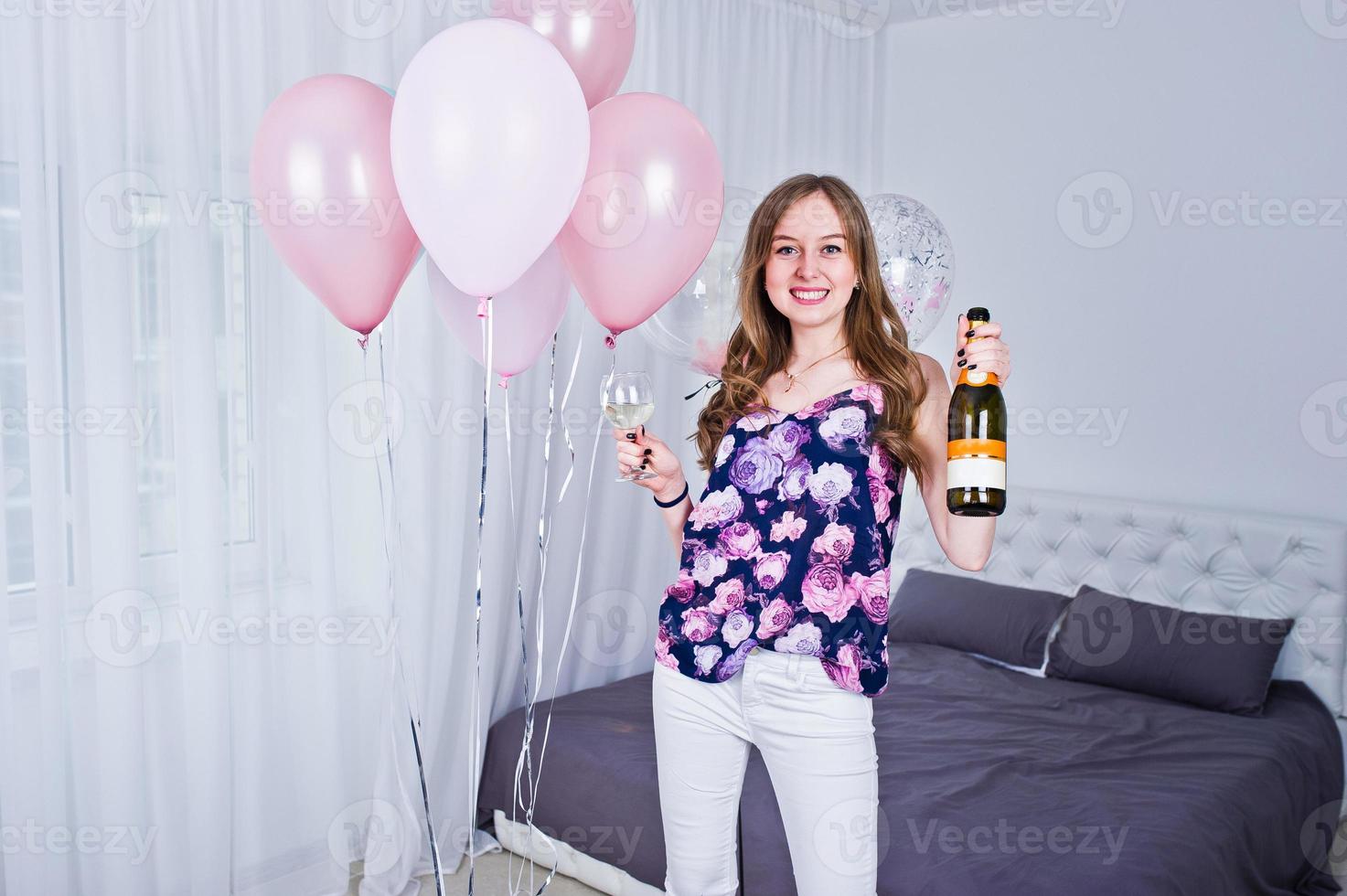 Happy girl with colored balloons on bed at room with glasses and bottle of champagne. Celebrating birthday theme. photo