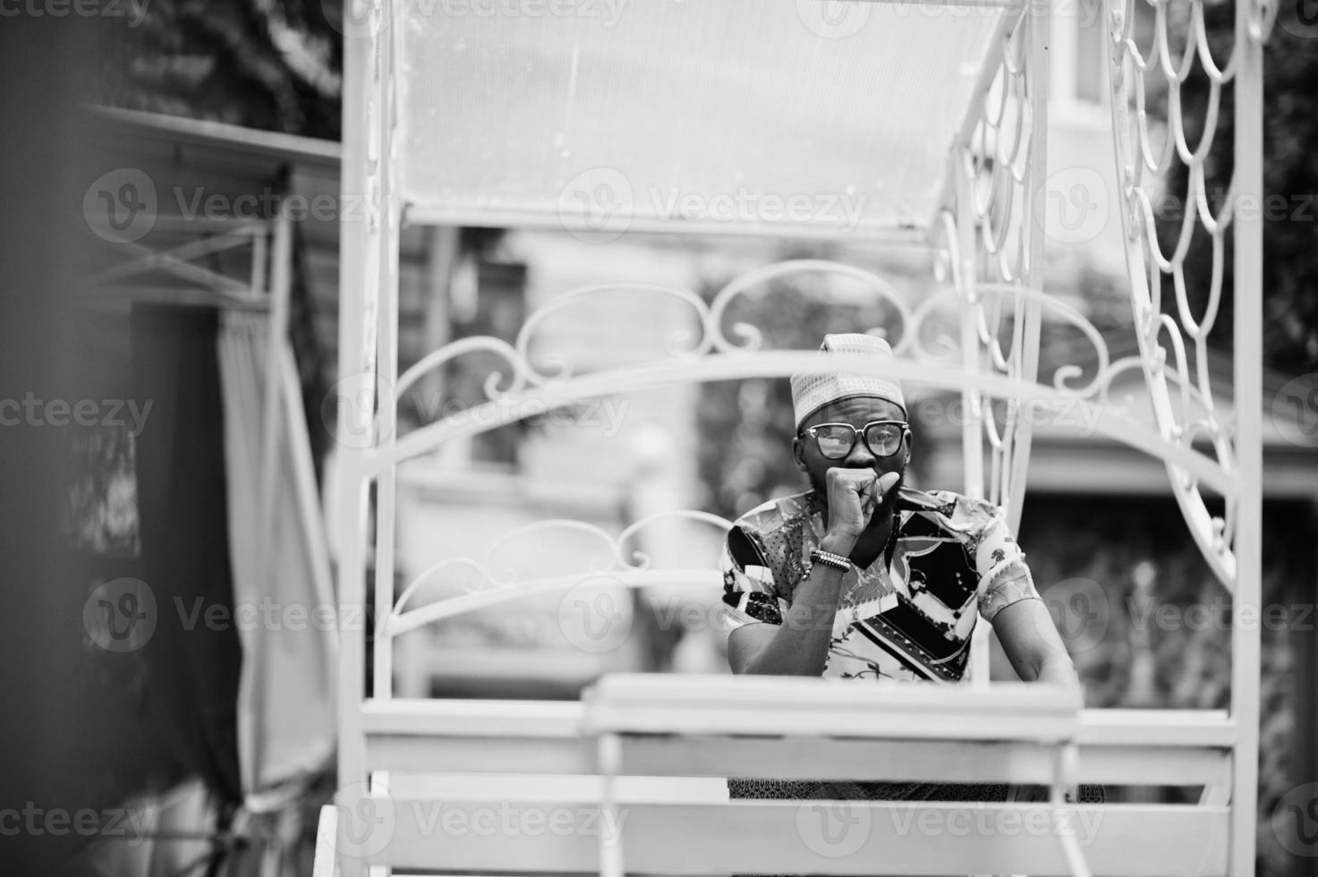 Handsome afro american man wearing traditional clothes, cap and eyeglasses sitting at white carriage. photo