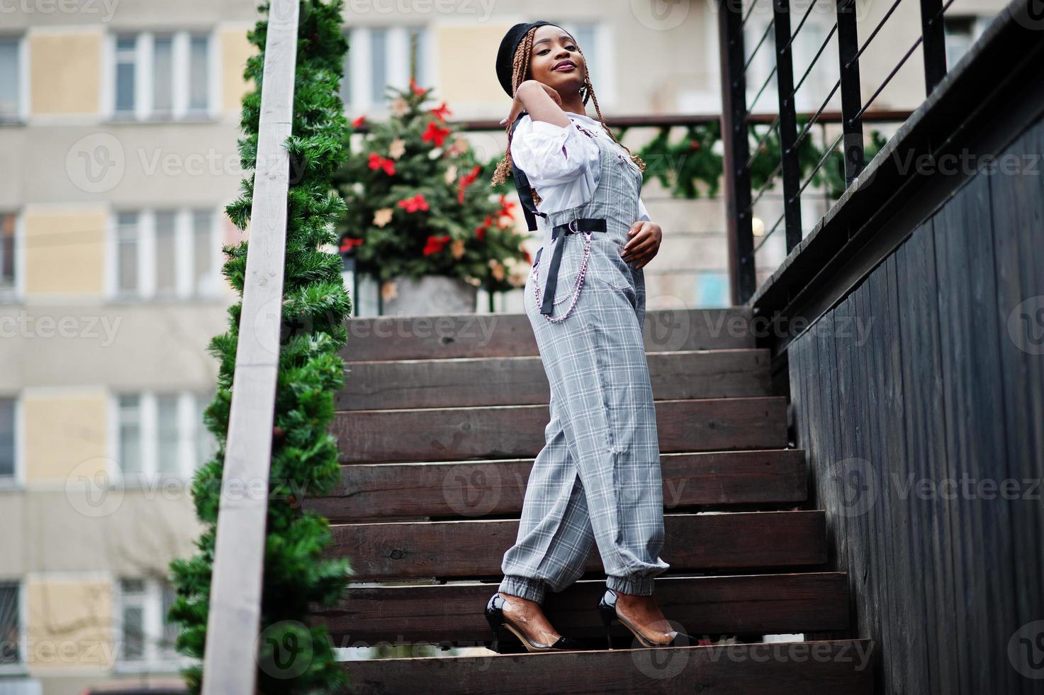 African american woman in overalls and beret posed in outdoor terrace with christmas decorations garland. photo