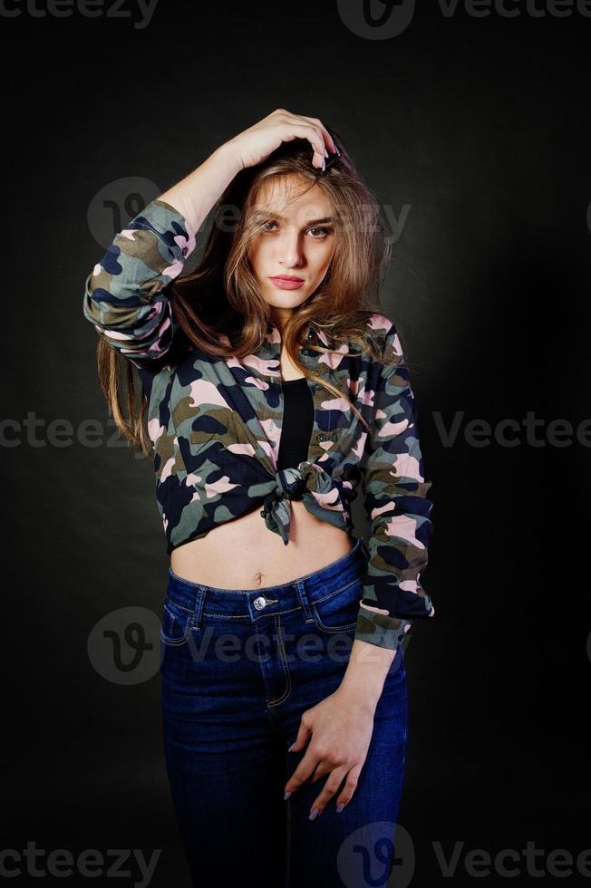 una guapa morena usa camisa militar y jeans, posando en el estudio con fondo gris. retrato de modelo de estudio. foto