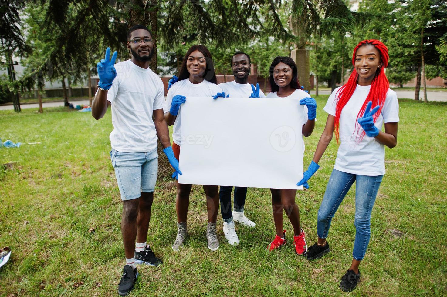 Group of happy african volunteers hold empty blank board in park. Africa volunteering, charity, people and ecology concept. Free space for your text. photo