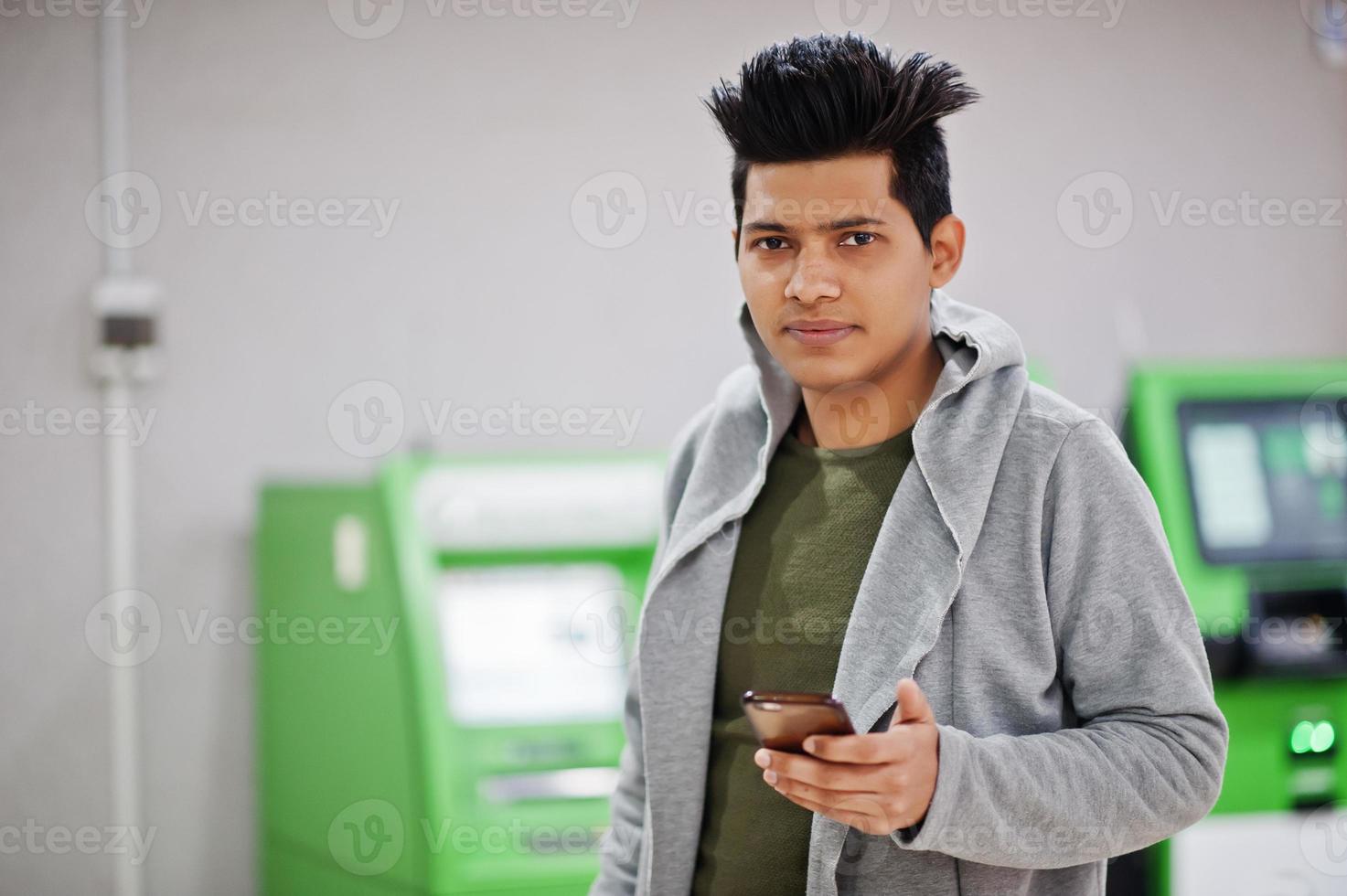 Young stylish asian man with mobile phone against row of green ATM. photo