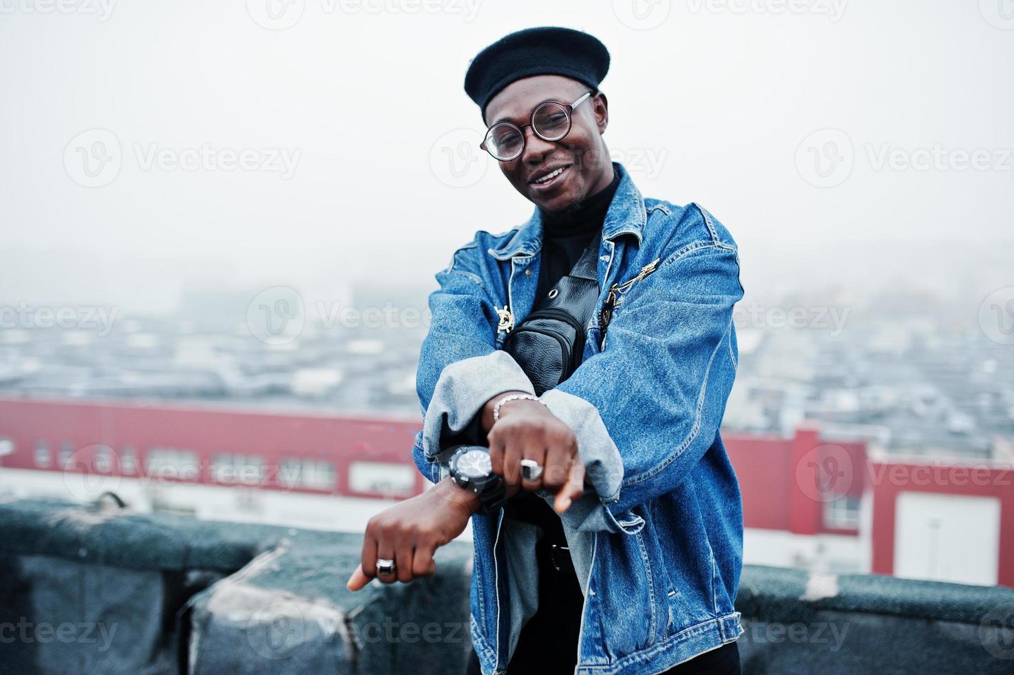 African american man in jeans jacket, beret and eyeglasses posed on abandoned roof. photo