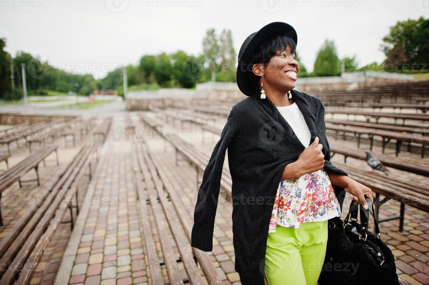 Amazing african american model woman in green pants and black hat posed at bench. photo