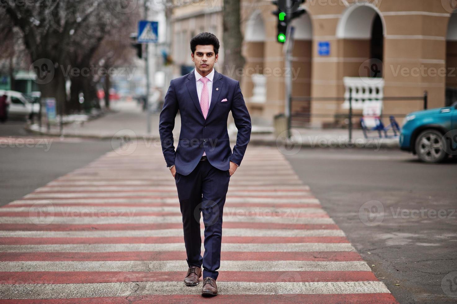 elegante modelo de hombre macho indio con traje y corbata rosa caminando en el cruce de peatones. foto