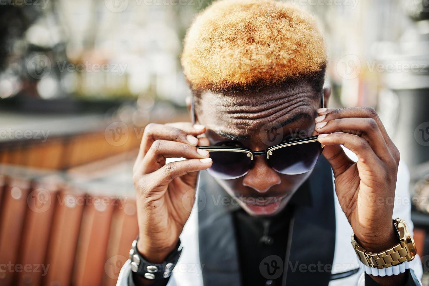 Chic handsome african american man in white suit and sunglasses sitting on bench. photo