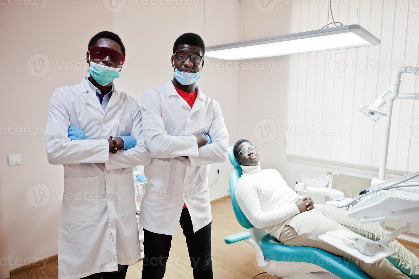 paciente afroamericano en silla dental. oficina de dentista y concepto de práctica médica. dos dentistas profesionales con las manos cruzadas en odontología médica. foto