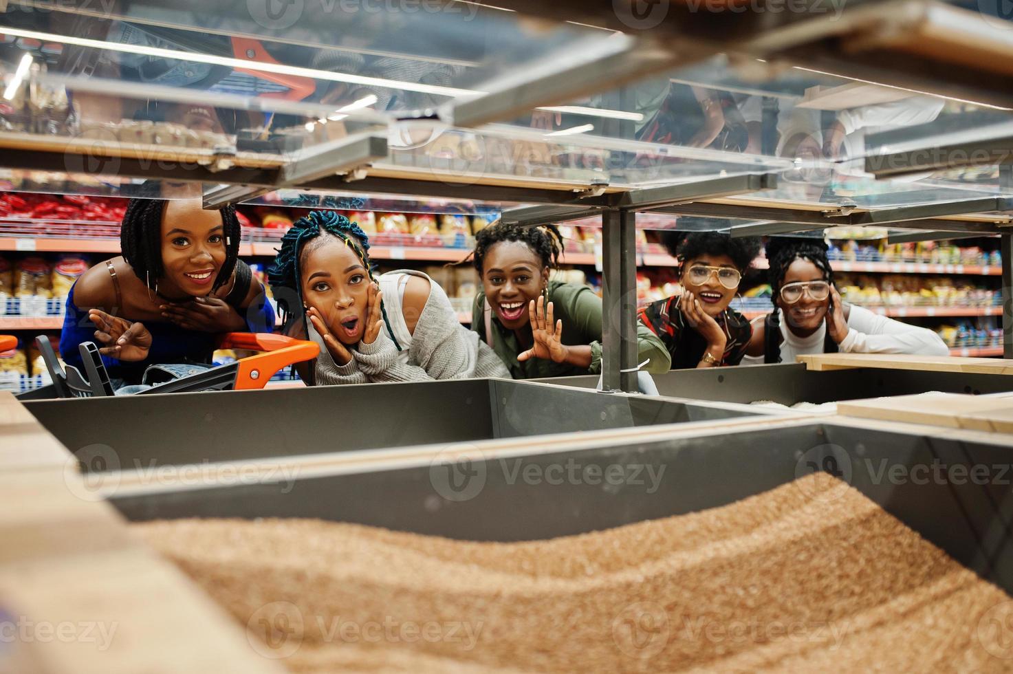 Group of five fun african womans with shopping carts choose buckwheat groats in supermarket. photo