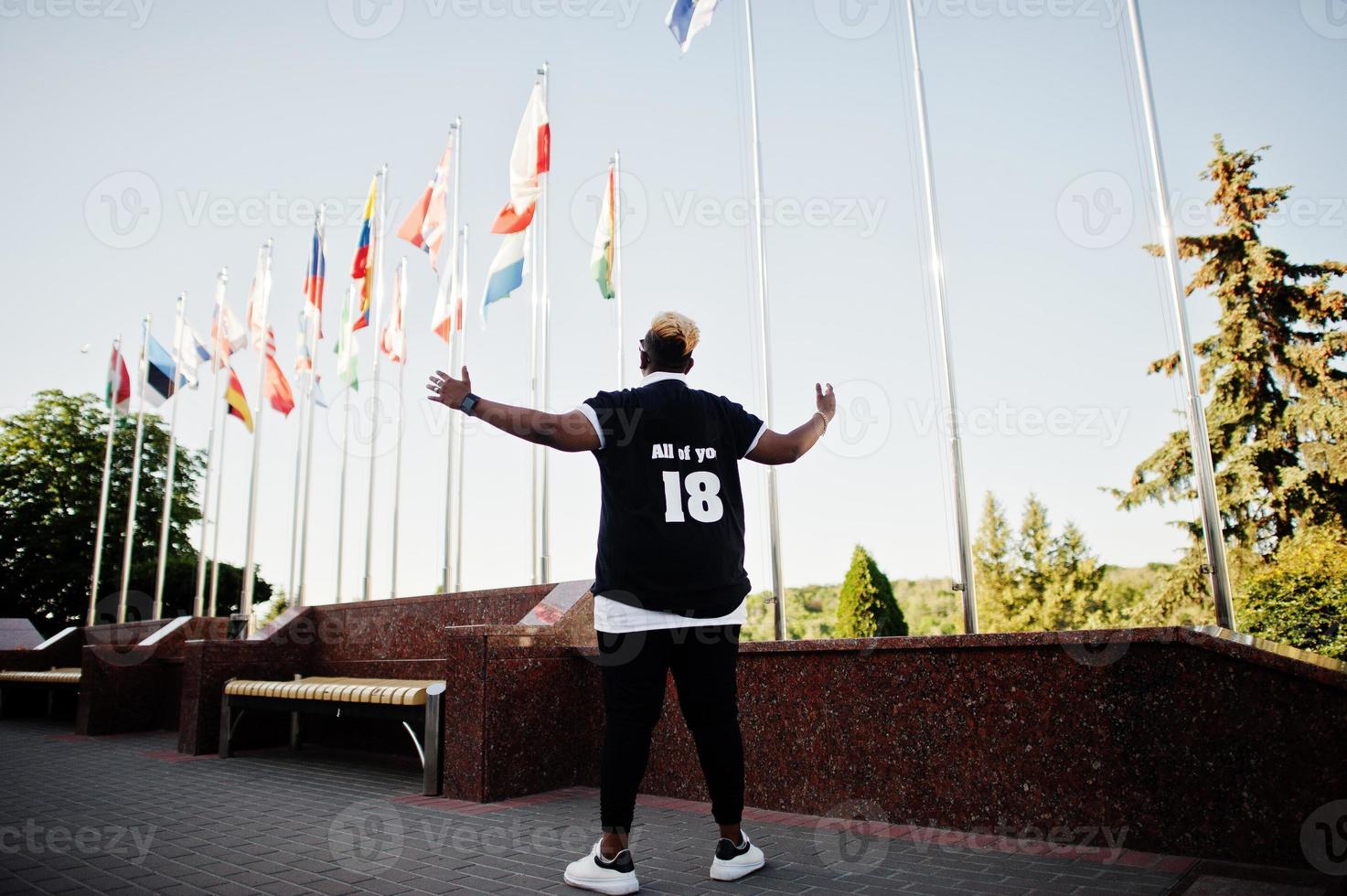 Stylish arabian muslim boy with originally hair posed on streets, against flags of different countries. photo