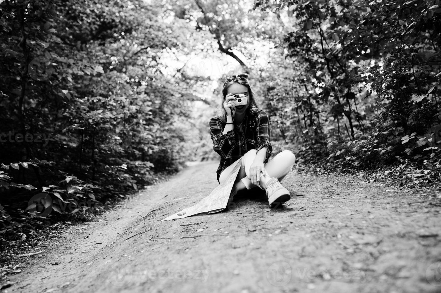 Portrait of an attractive blond girl with a map sitting in the forest and taking photos. photo