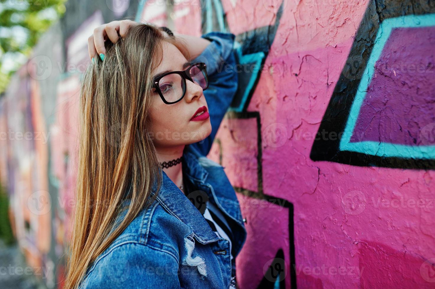 Stylish casual hipster girl in jeans wear and glasses against large graffiti wall. photo