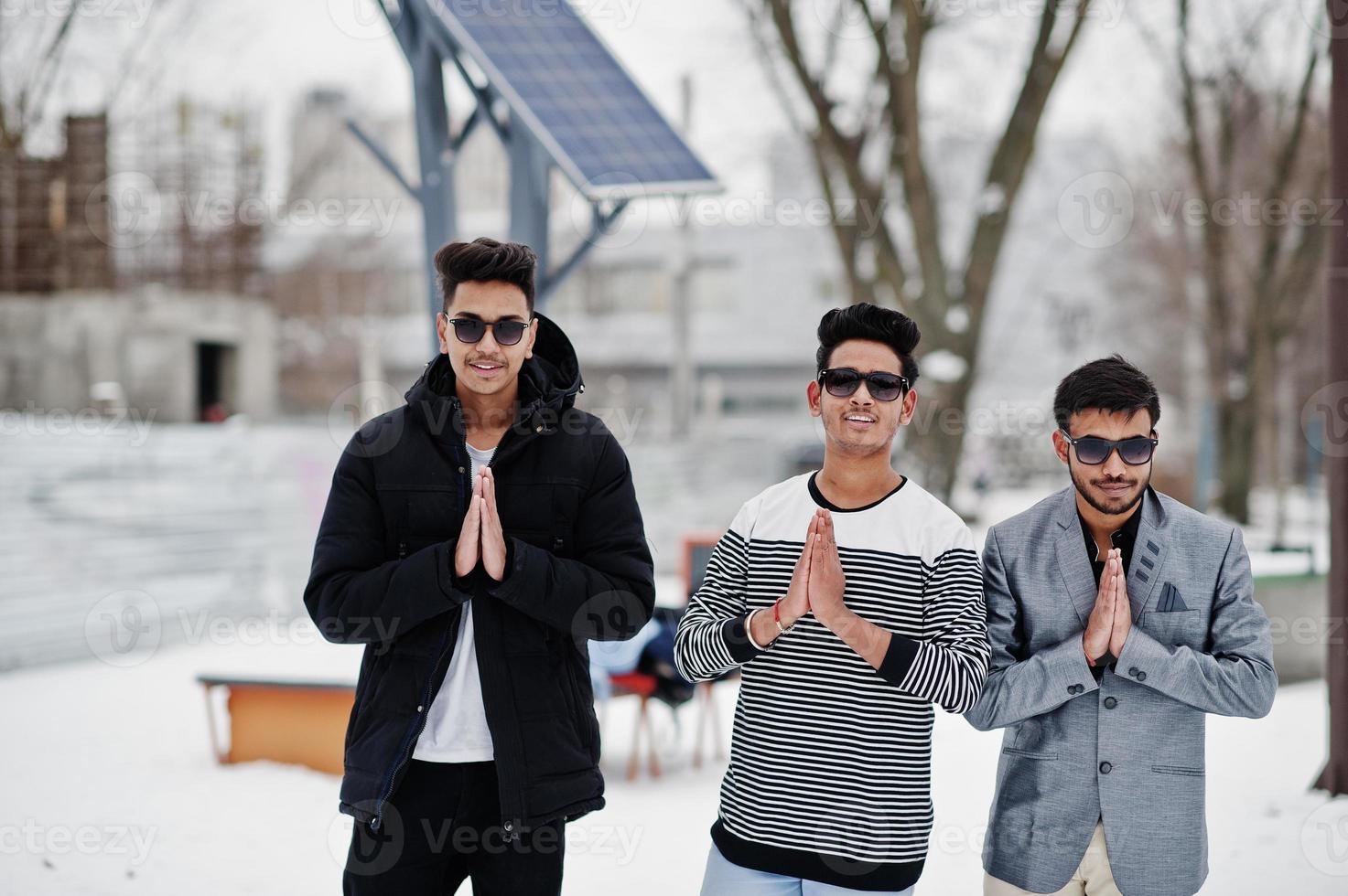 Group of three casual young indian mans in sunglasses posed at winter day, shows namaste. photo