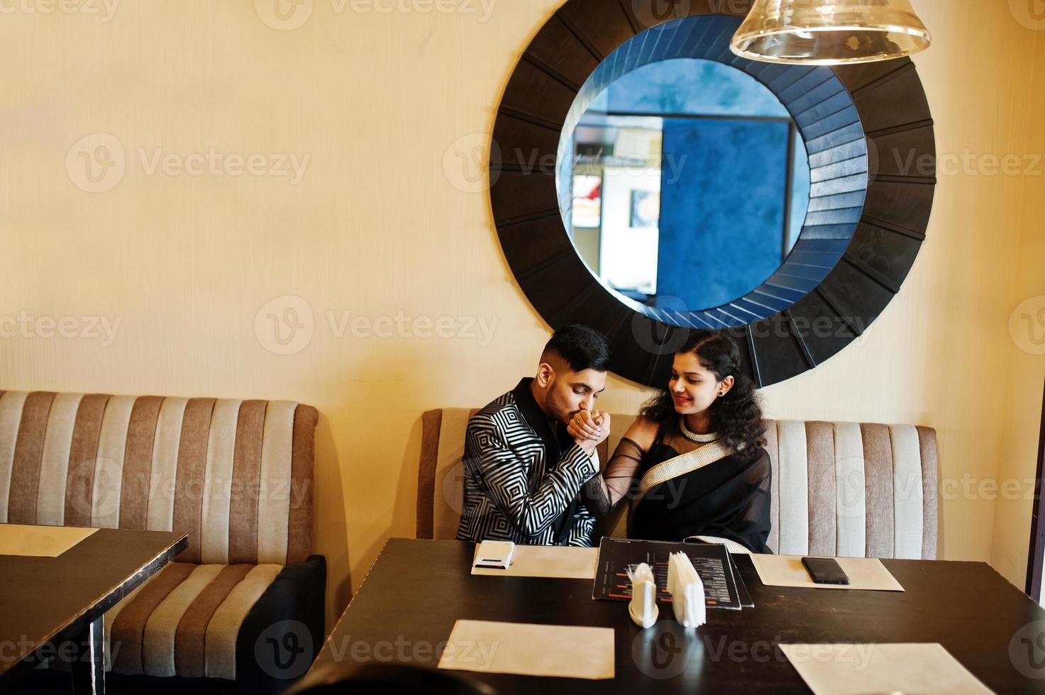 Lovely indian couple in love, wear at saree and elegant suit, posed on restaurant. Man kissing her hand. photo