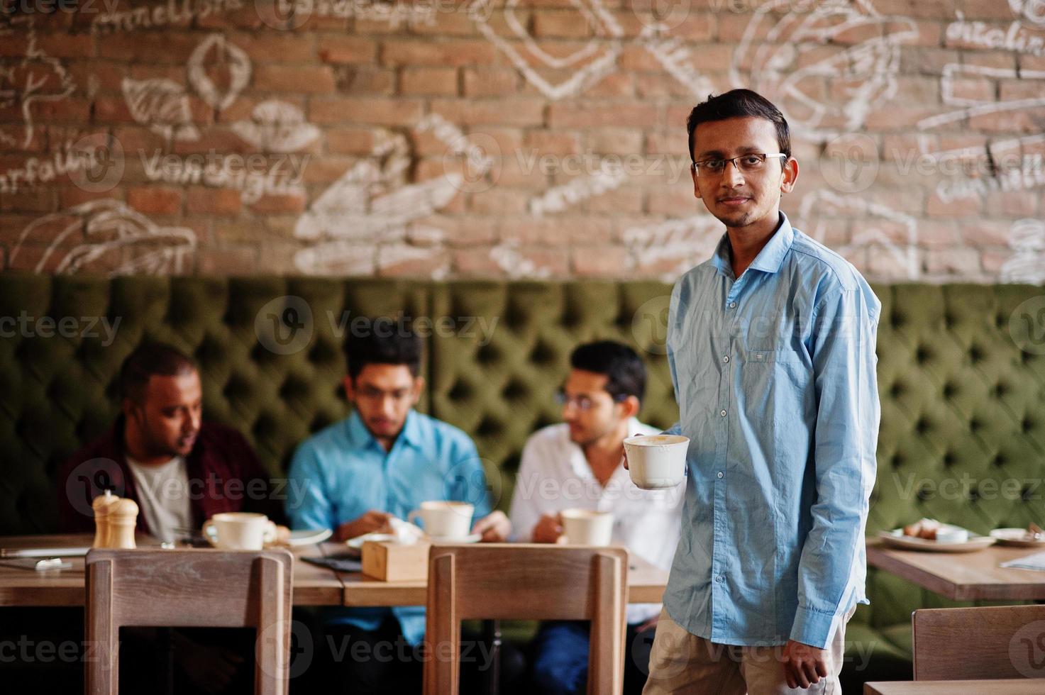 Group of four south asian men's posed at business meeting in cafe. Indians work together, having conversation. Indian man with cup of coffee. photo