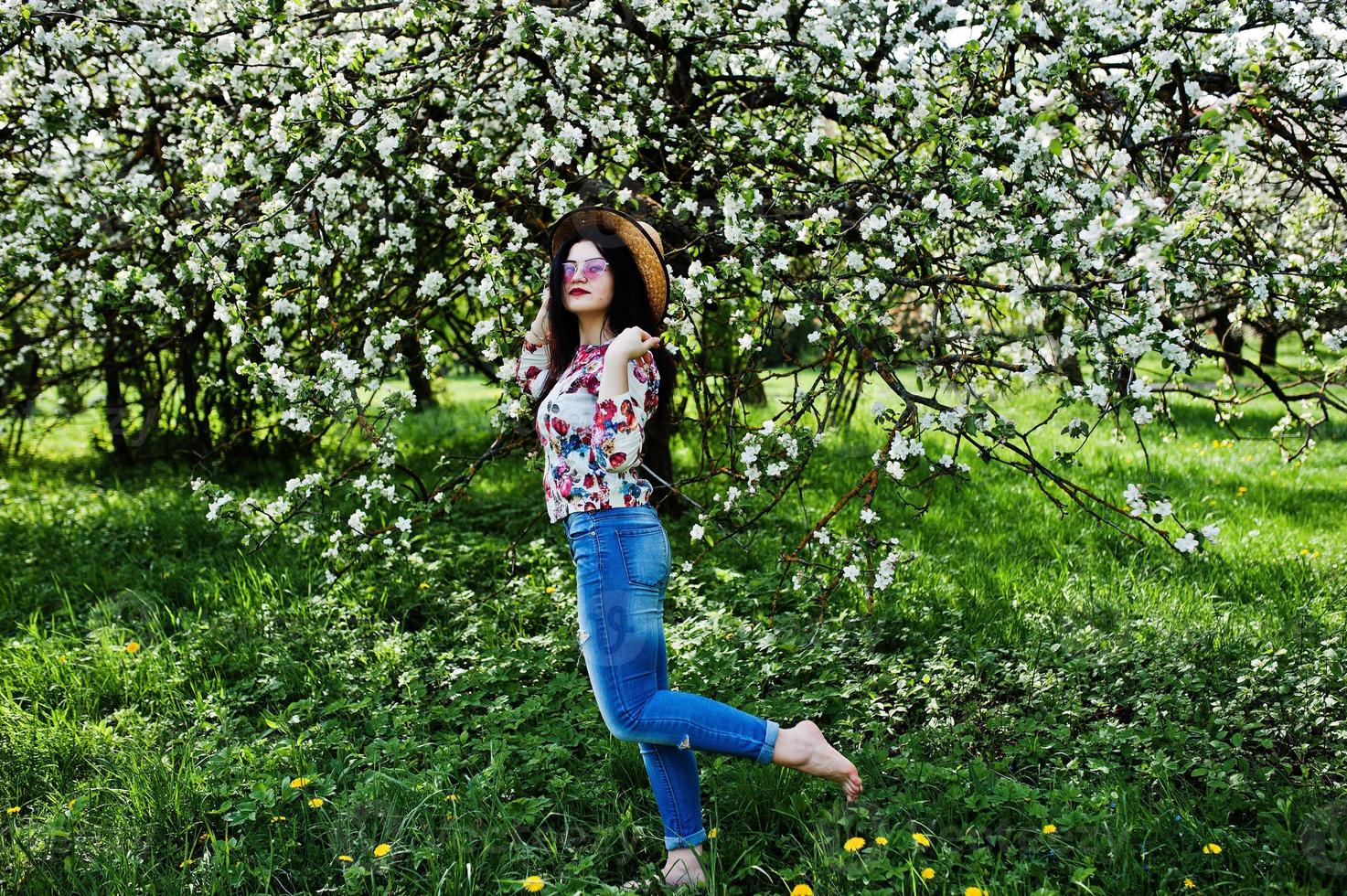 Spring portrait of brunette girl in pink glasses and hat at green blossom garden. photo