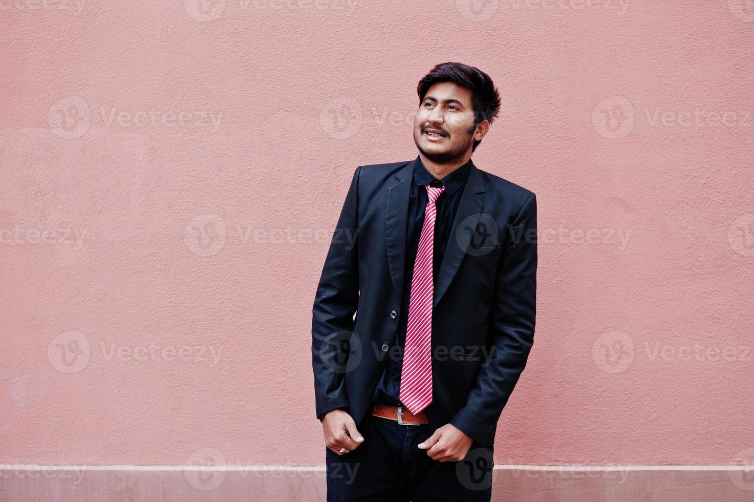 Young indian man on suit and tie posed against pink wall. photo