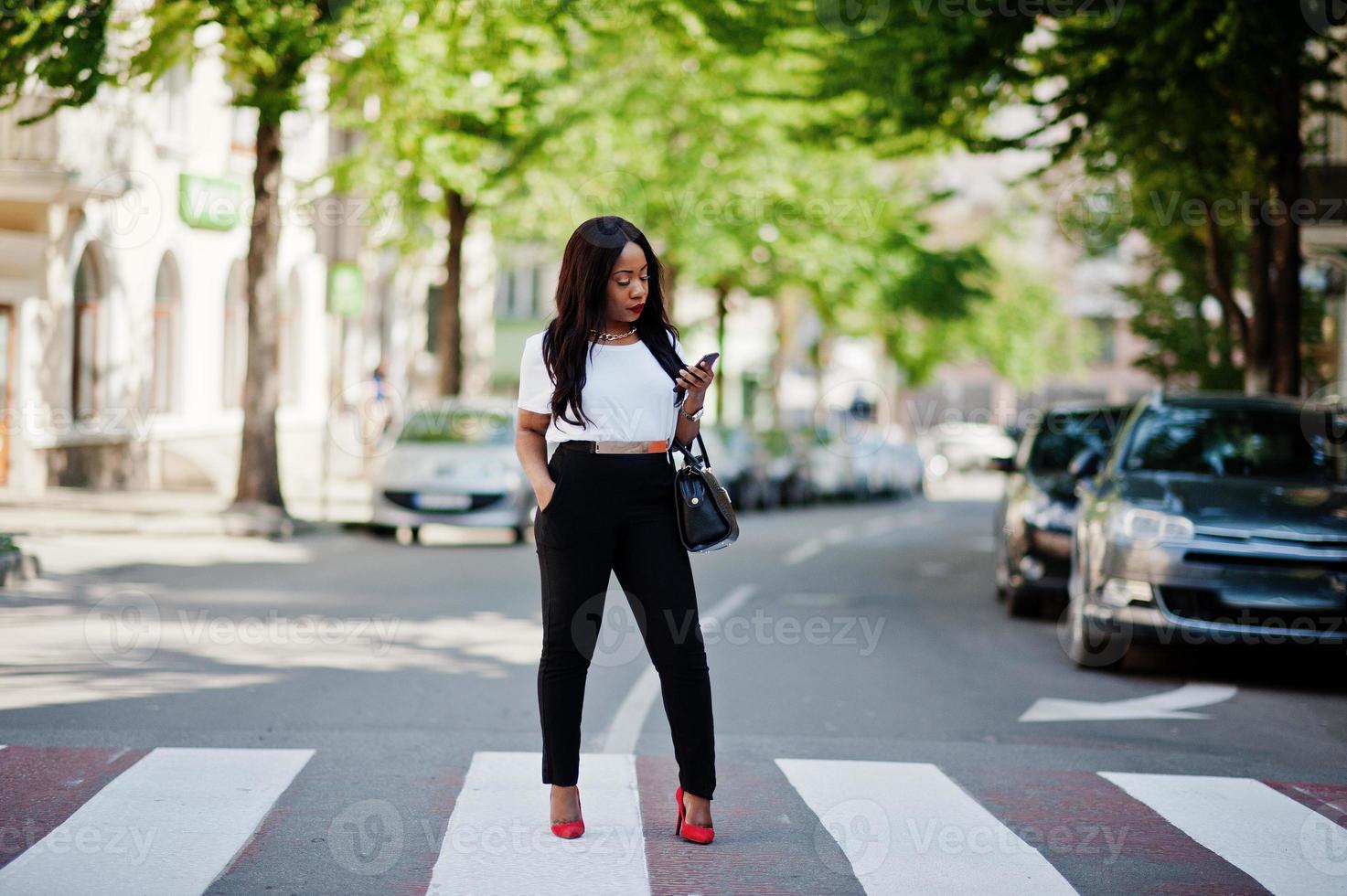 Stylish african american business woman on streets of city at pedestrian crossing. photo