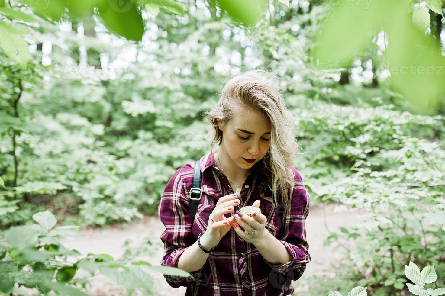 retrato de una atractiva chica rubia posando con una brújula en un bosque. foto