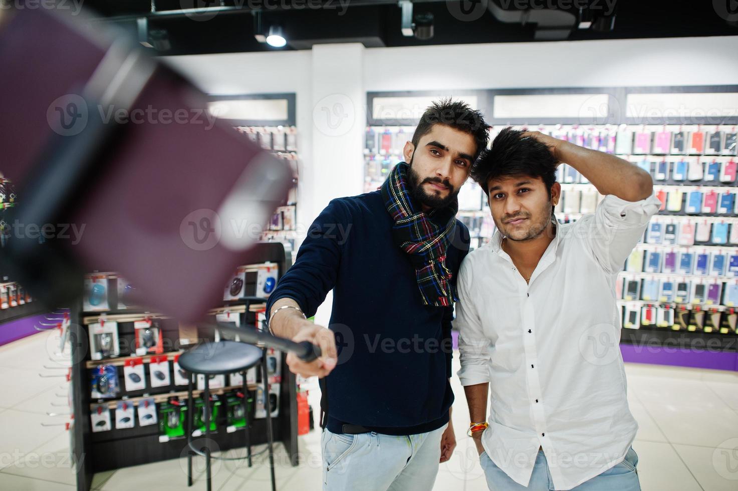 Two indians mans customer buyer at mobile phone making selfie by monopod stick. South asian peoples and technologies concept. Cellphone shop. photo