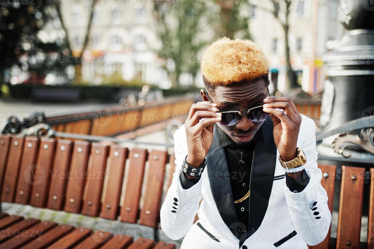 Chic handsome african american man in white suit and sunglasses sitting on bench. photo