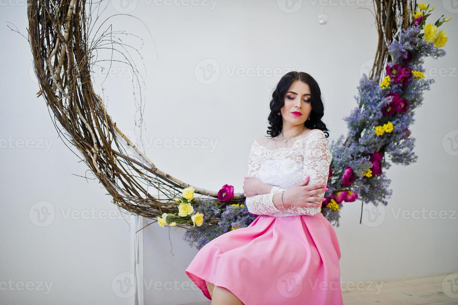 Young brunette girl in pink skirt and white blouse posed indoor against large decorated wreath. photo
