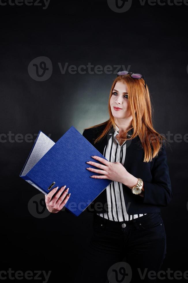 retrato de una mujer de negocios pelirroja con blusa a rayas, gafas y una chaqueta con una carpeta azul. foto