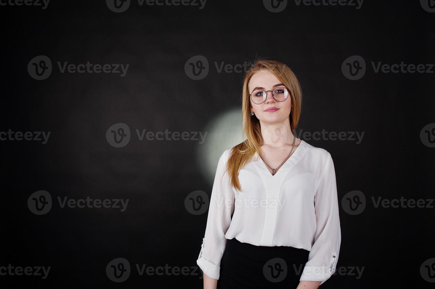 Studio portrait of blonde businesswoman in glasses, white blouse and black skirt against dark background. Successful woman and stylish girl concept. photo