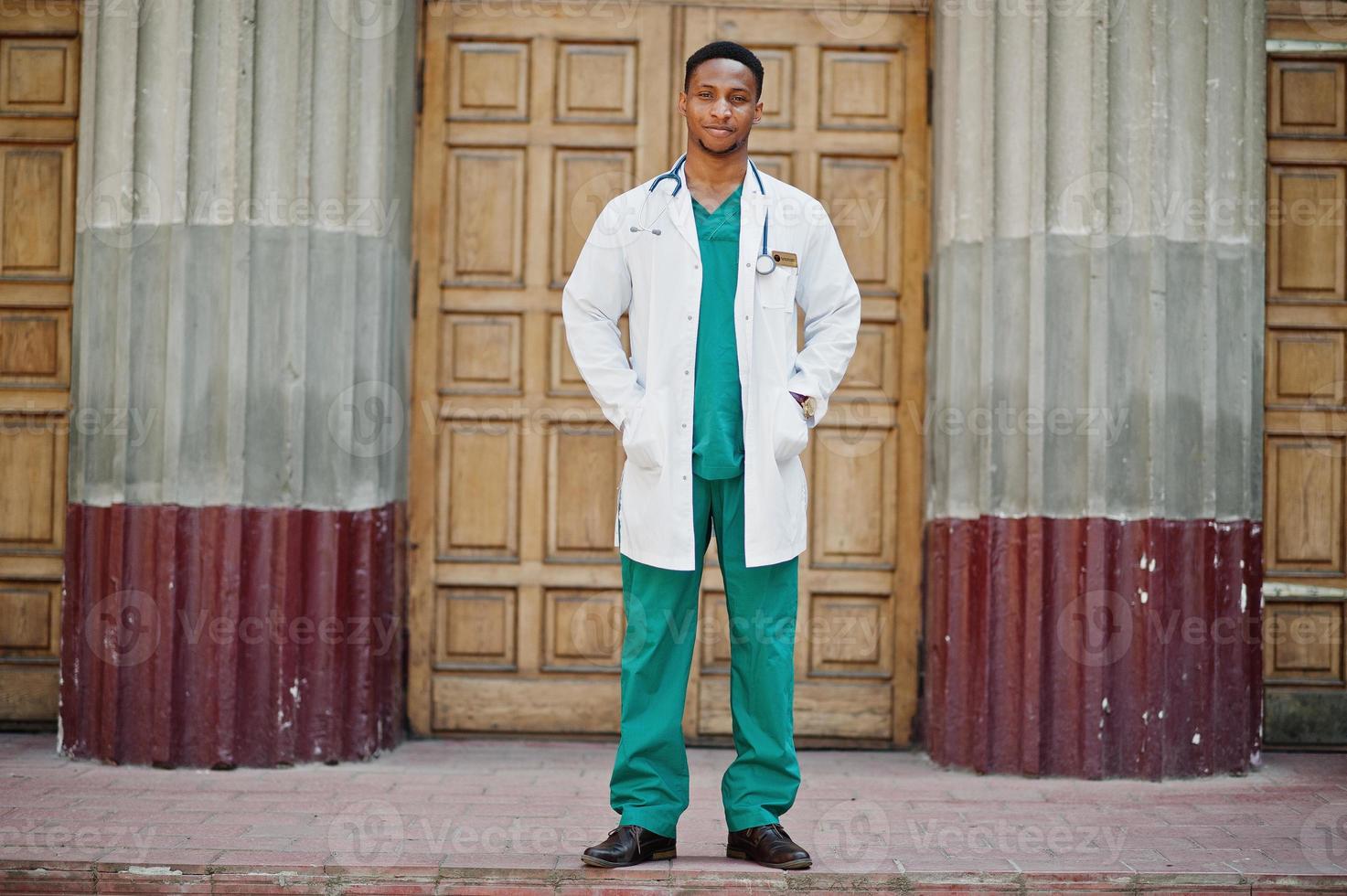 African american doctor male at lab coat with stethoscope outdoor against clinic door. photo